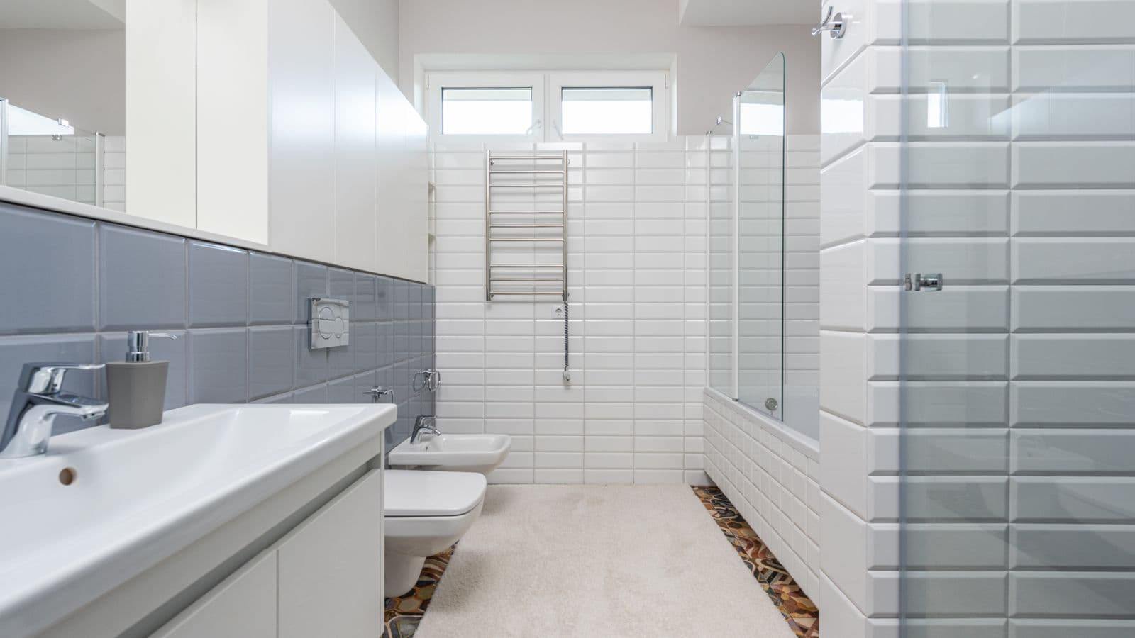 A white tiled bathroom with a wall-hung toilet, a bidet and a heated towel rail