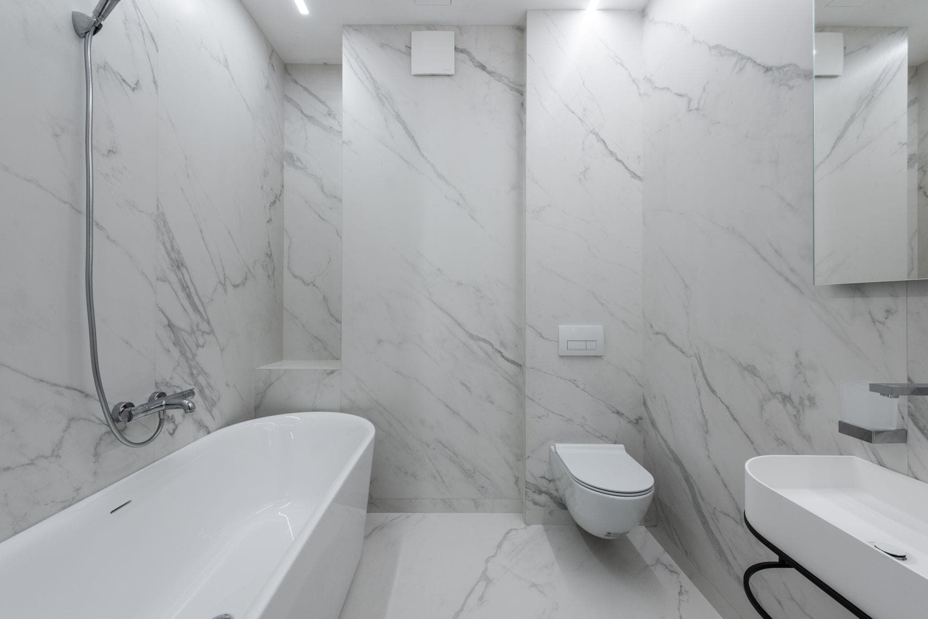 A white marble bathroom with a wall-hung toilet, a flush plate and a freestanding bath