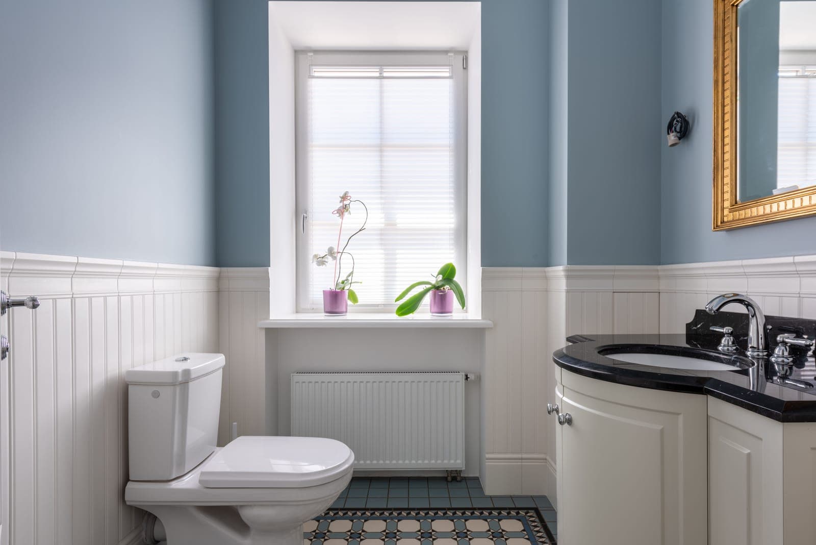 A two-piece toilet with a closed seat in a blue and white bathroom, beside a vanity and a window