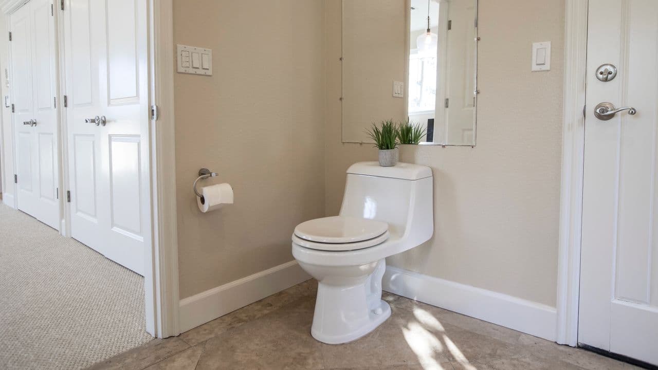 A plain white one-piece toilet in a beige bathroom with a paper holder on the wall