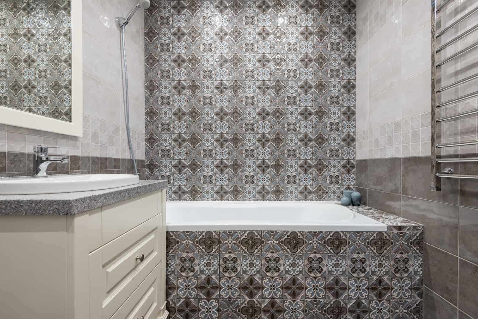 A patterned tiled bathroom with a handheld shower on a hose above the bath