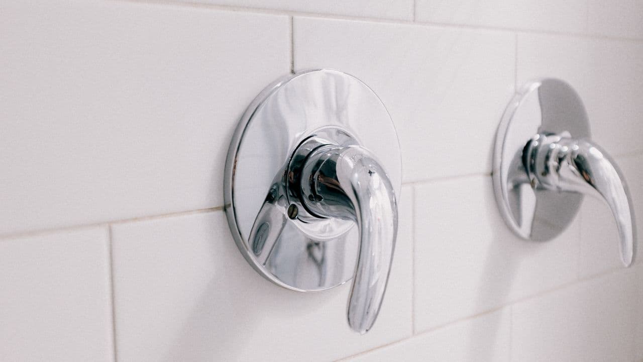 Two chrome shower control handles on a white tiled bathroom wall
