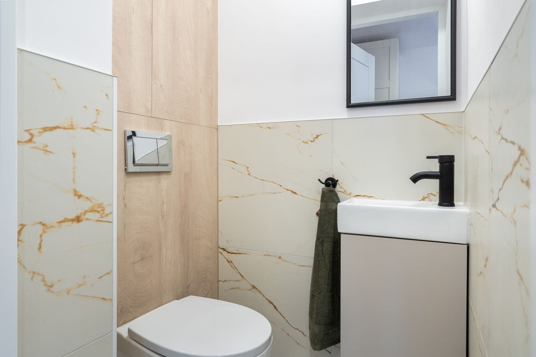 A compact toilet with a two-button chrome flush plate on a marble-tiled wall