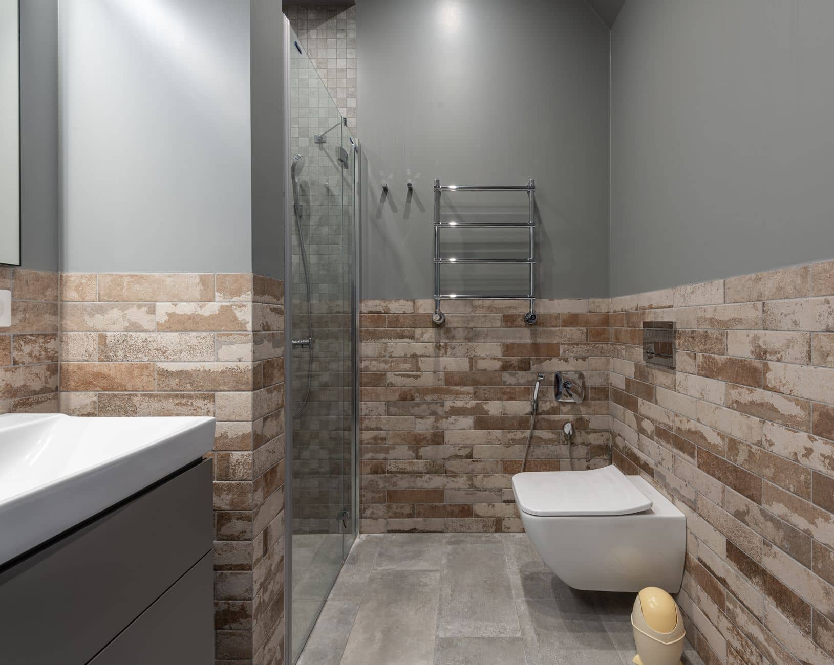 A wall-hung toilet beside a glass shower in a brick-tiled bathroom