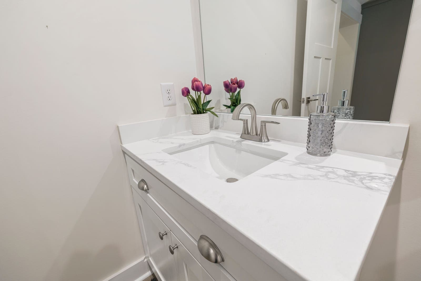 A two-handle brushed nickel faucet on a white quartz vanity with an undermount basin