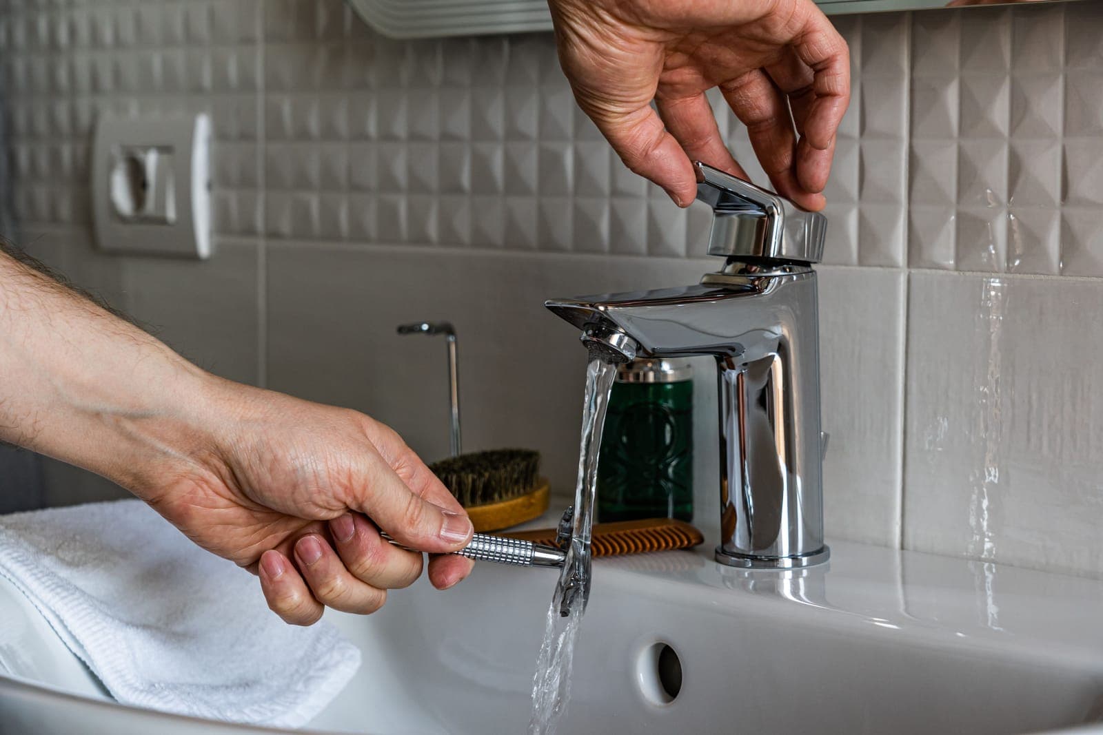 Hands rinsing a razor under a single-lever chrome basin faucet