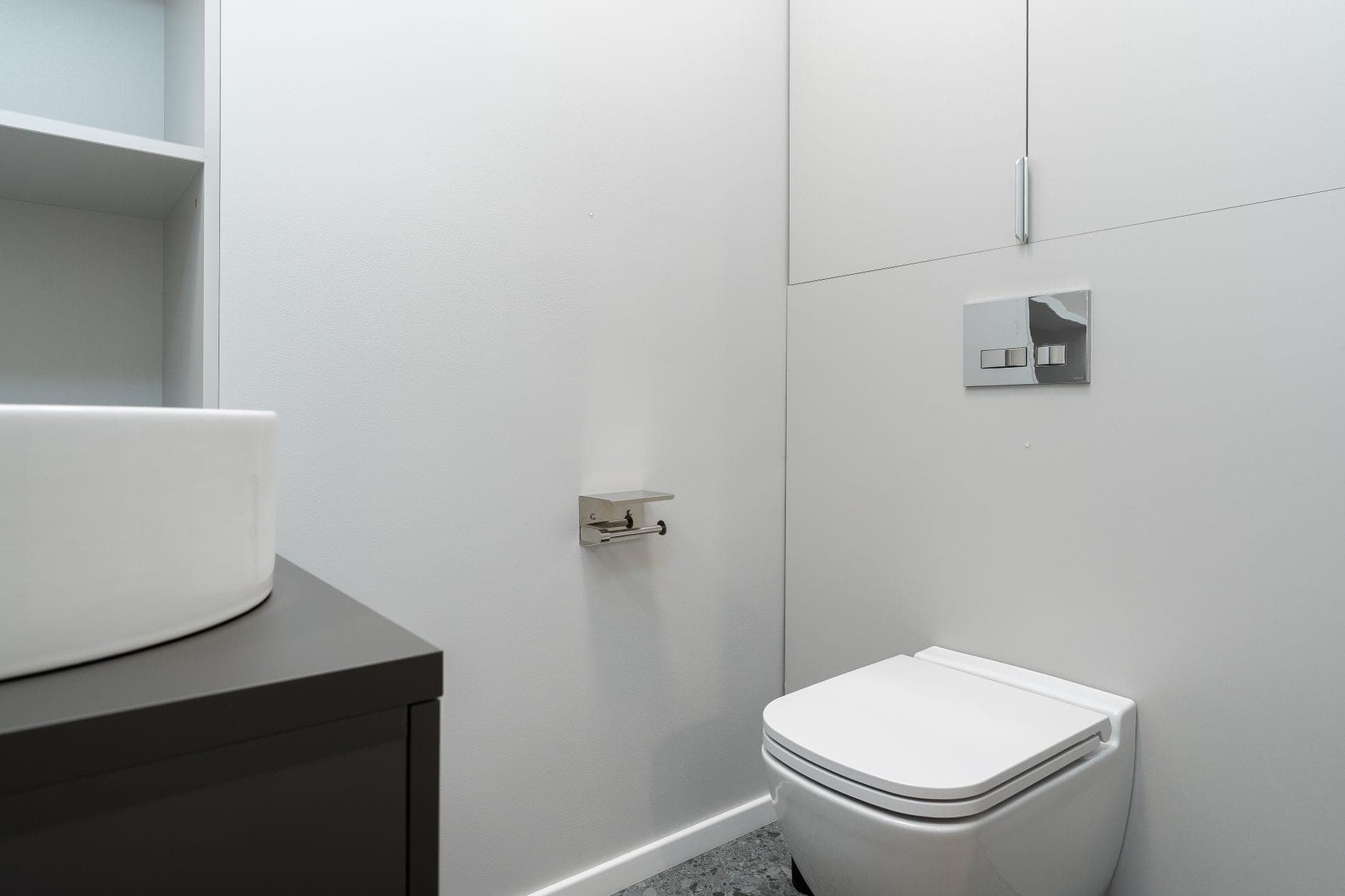A wall-hung toilet with a chrome flush plate in a white bathroom