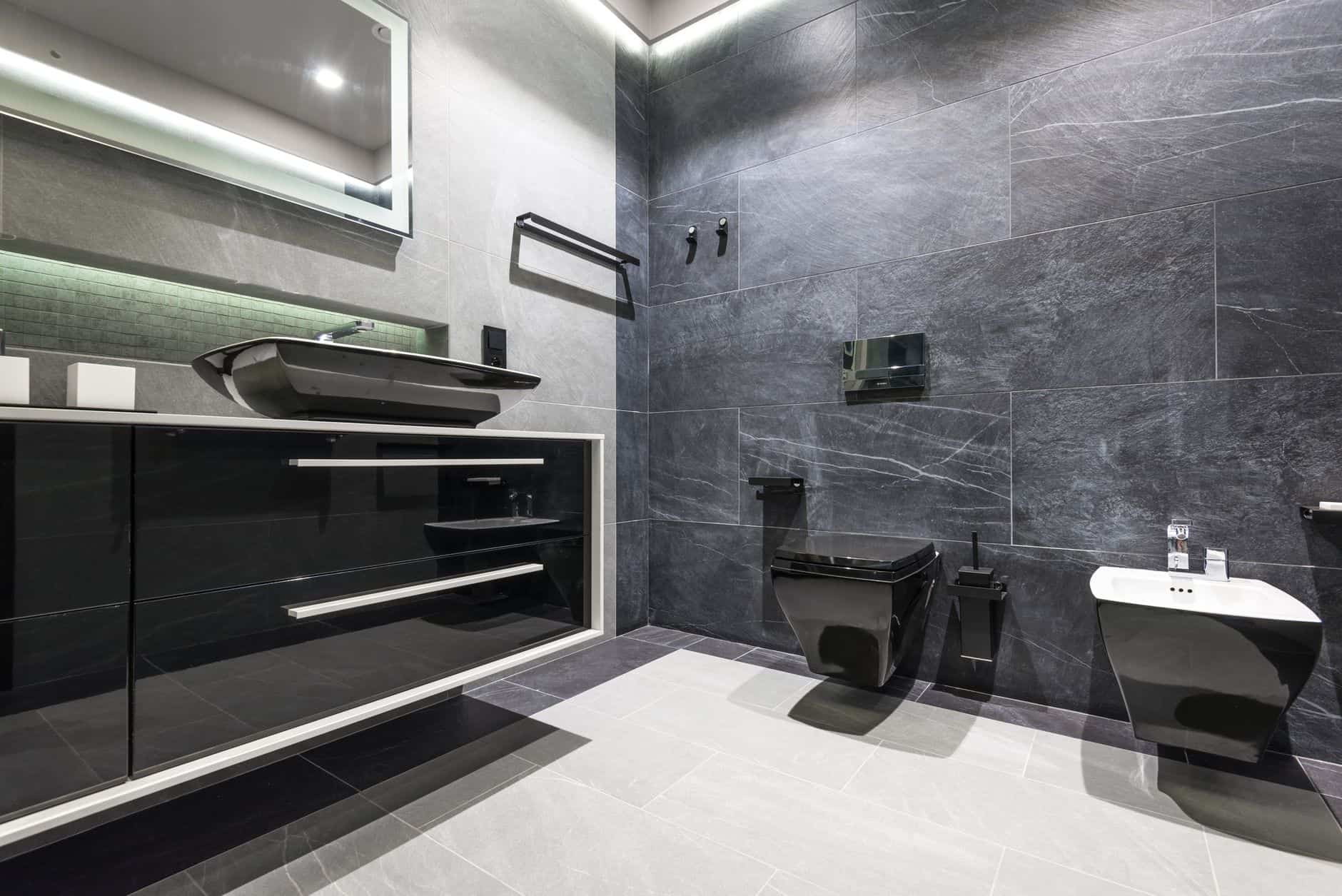 A dark tiled bathroom with a black wall-hung toilet and matching basin