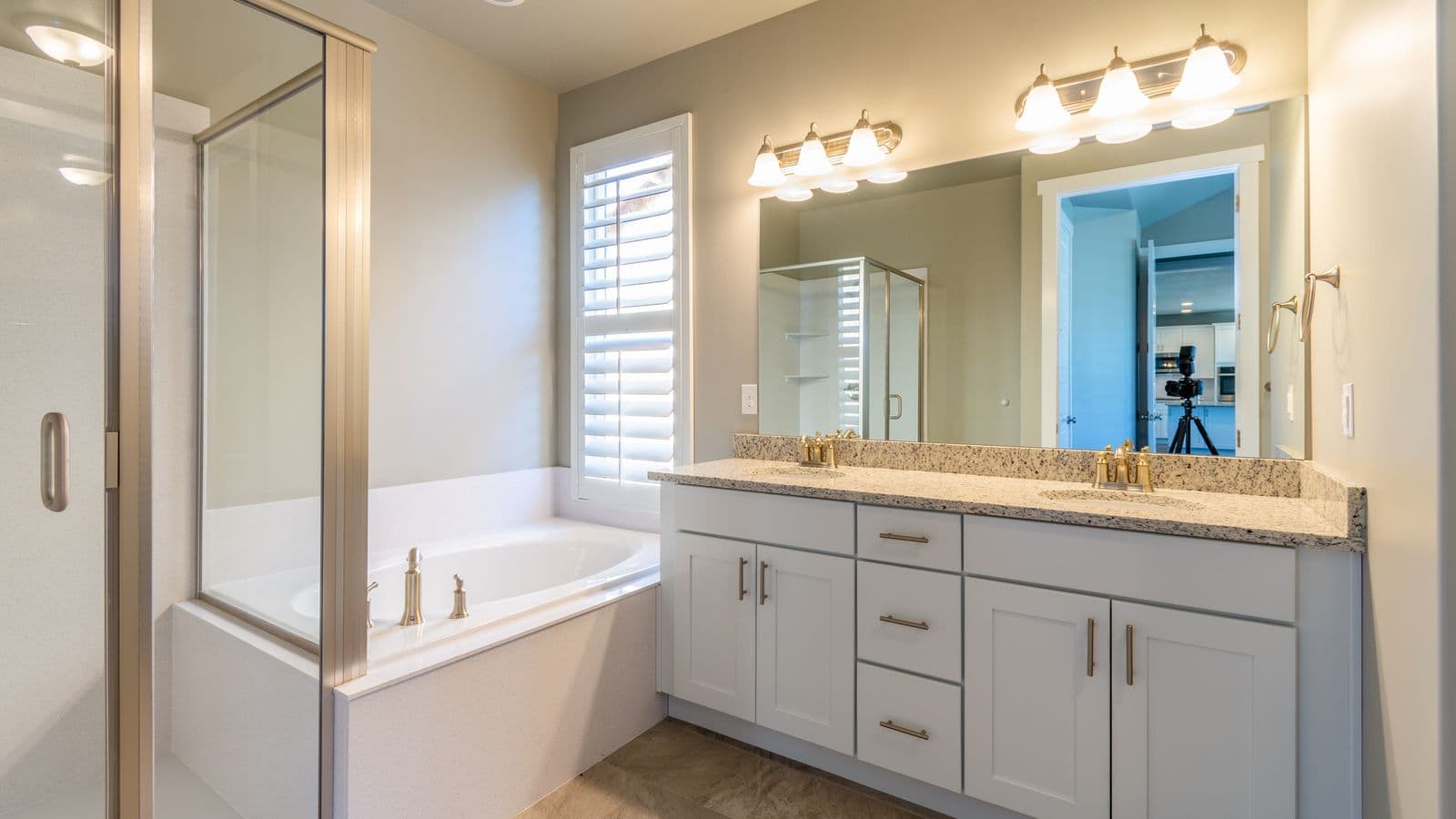 A bright bathroom with a double vanity, large mirror, vanity lights, tub and glass shower