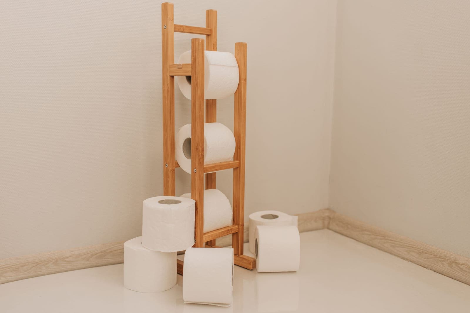A freestanding bamboo toilet roll stand holding three rolls, with spare rolls stacked on the floor