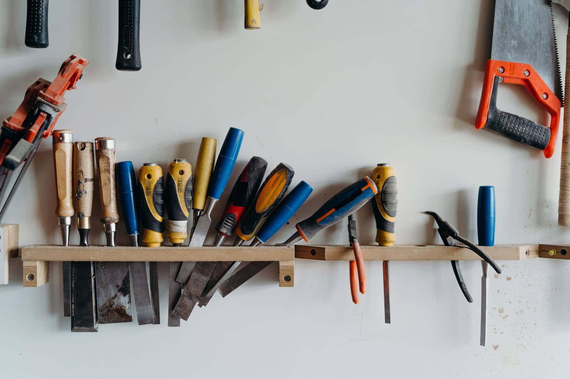 Screwdrivers, chisels and a saw hanging on a workshop wall rack