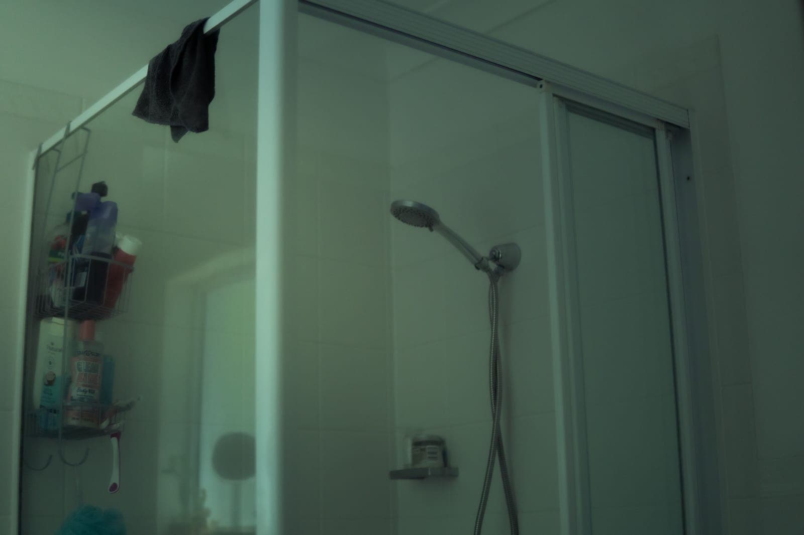 A hanging caddy full of bottles on the frame of a glass shower door, with a towel over the top edge
