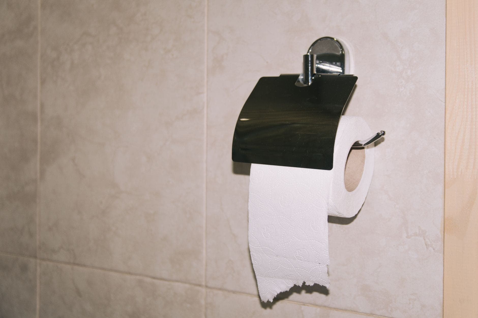 A chrome toilet paper holder with a cover mounted on a tiled wall