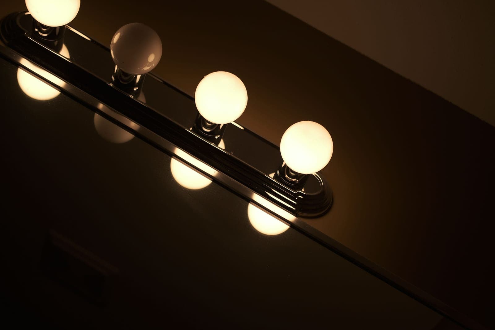 A vanity light bar with warm globe bulbs above a bathroom mirror, one bulb unlit