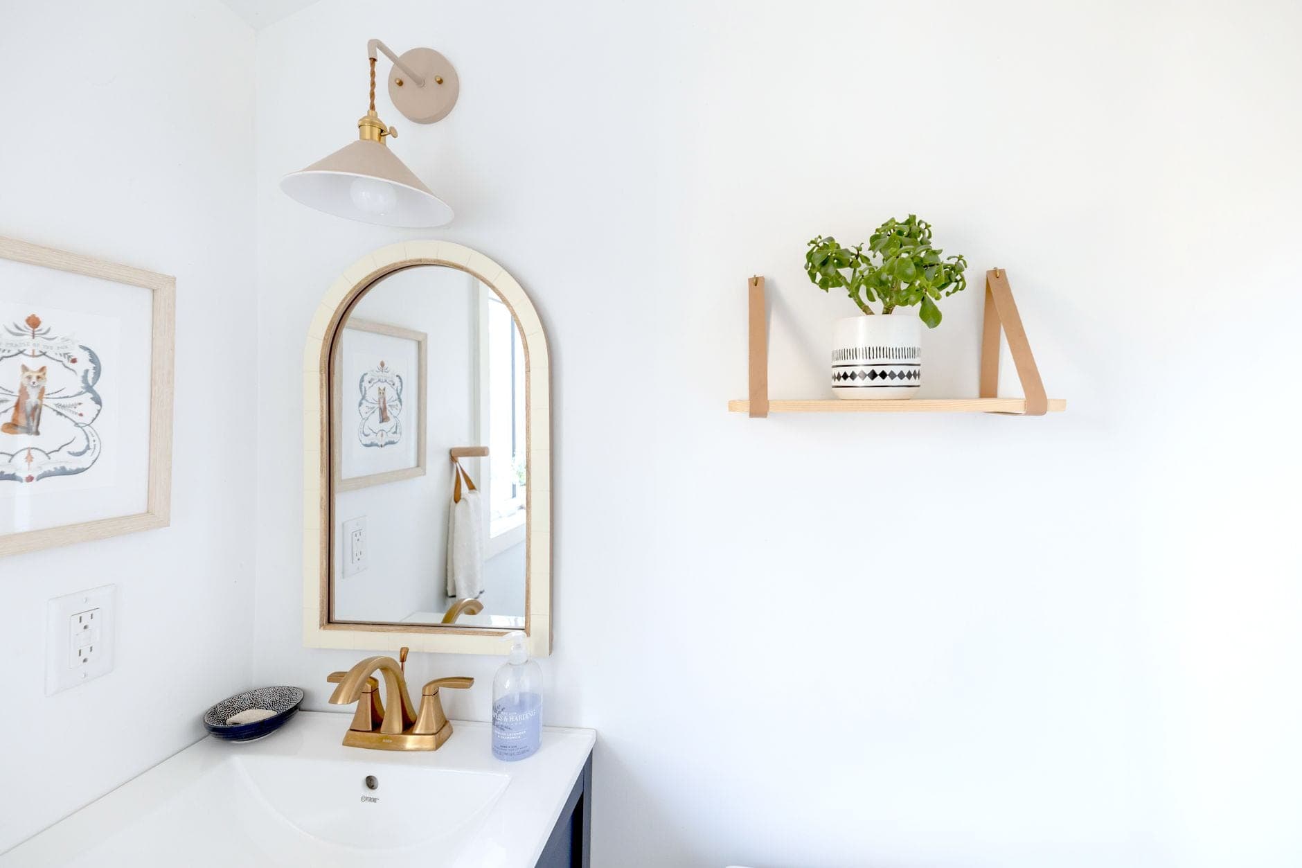 A wall sconce above an arched mirror over a white bathroom sink