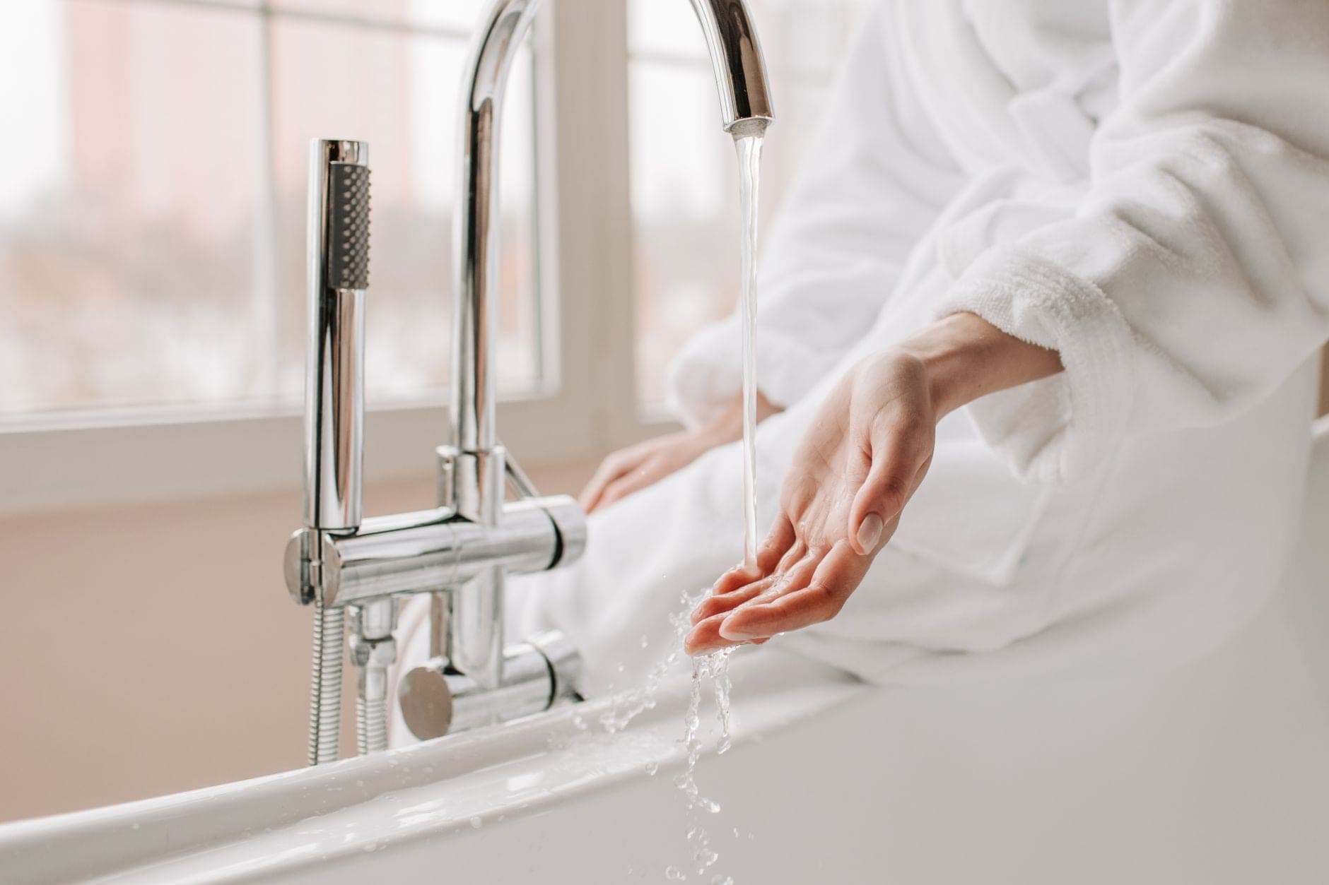 Water running from a chrome bath faucet with a handheld shower on the tub rim