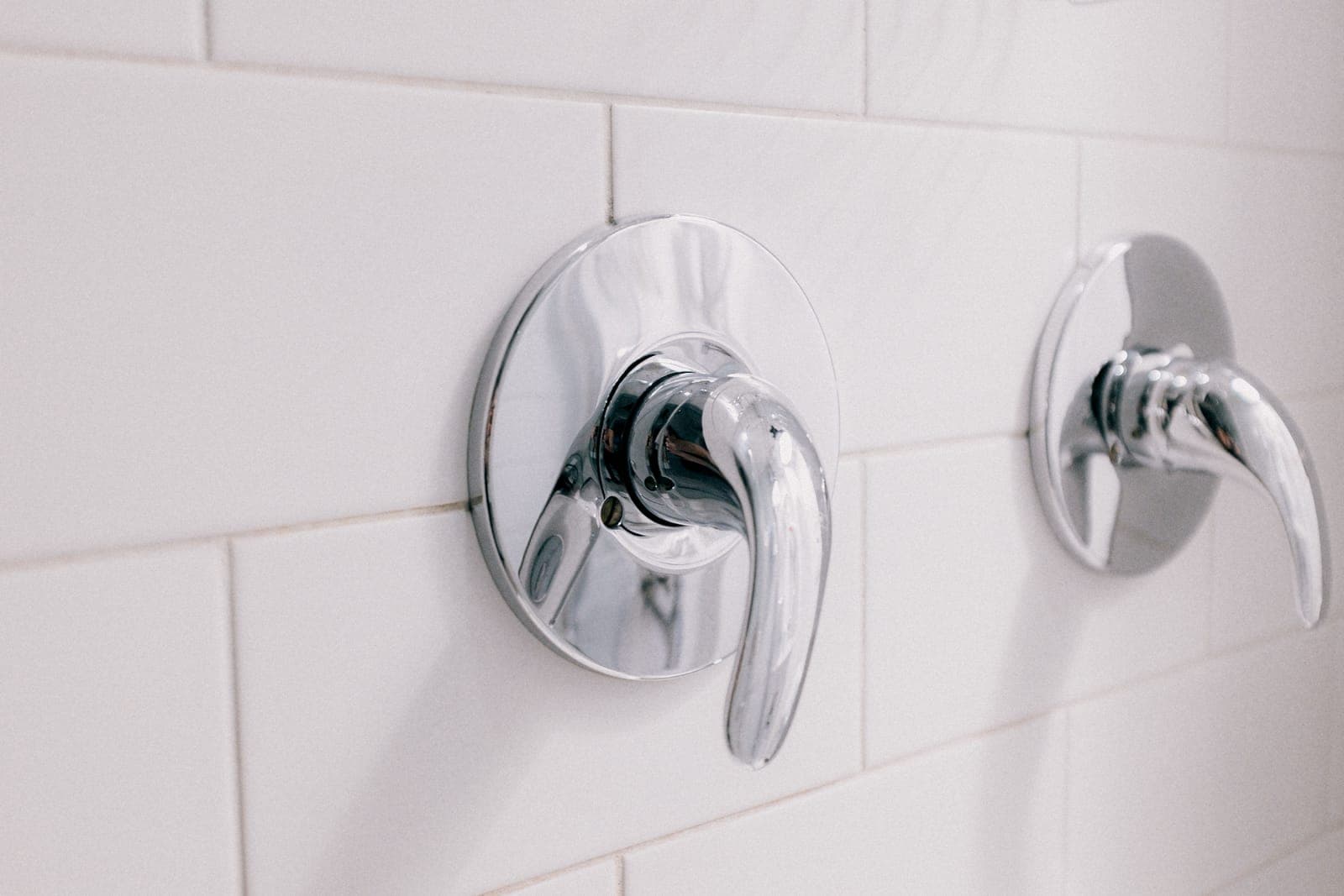 Two chrome shower mixer levers mounted on a white tiled wall