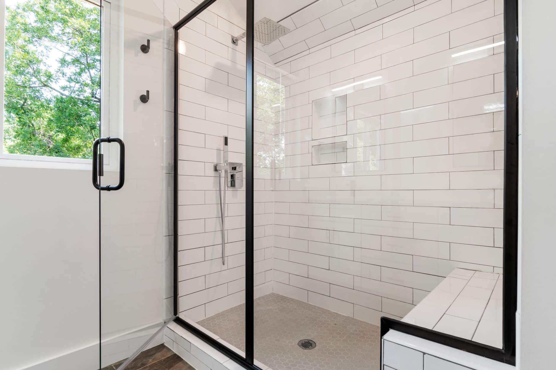 A white-tiled shower with a square rain head and a handheld shower behind a glass door