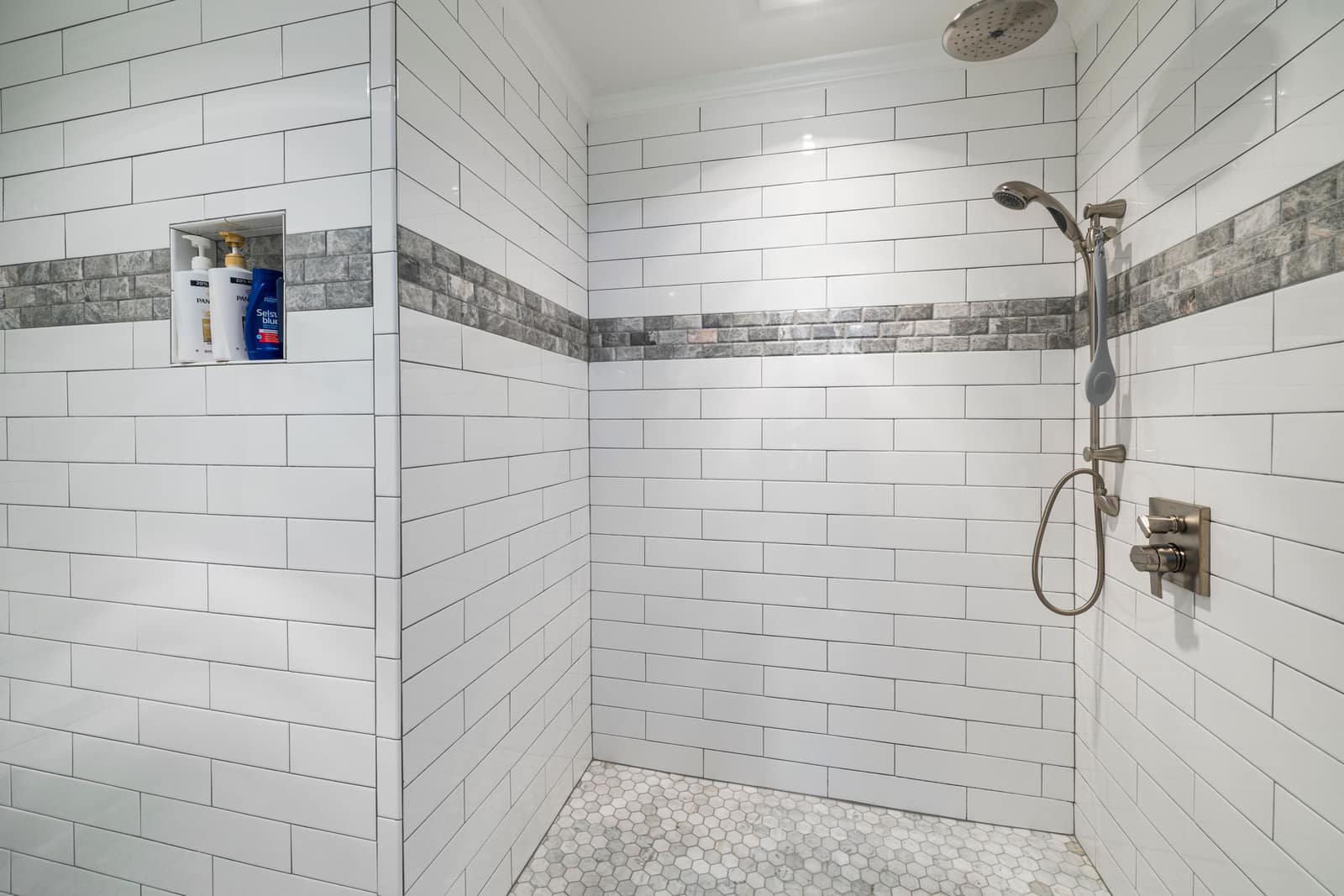 A white tiled shower with a fixed overhead head and a handheld shower on a hose beside the mixer
