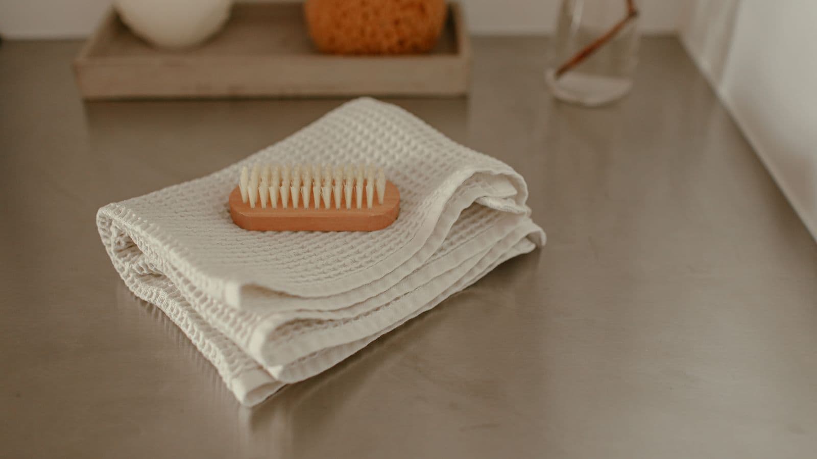 A folded cream waffle-weave towel on a counter with a wooden nail brush resting on it
