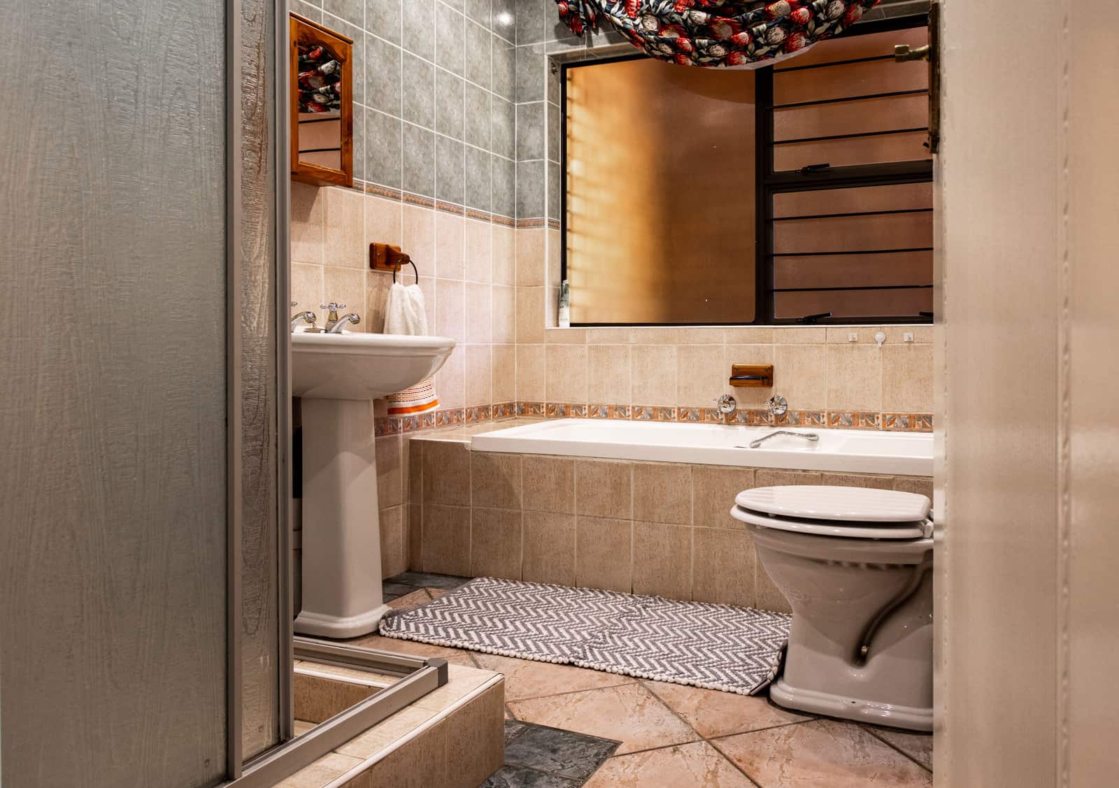 A woven gray and white cotton bath mat on the tiled floor beside a bath