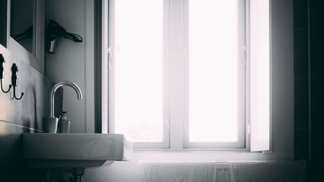 A white basin beside a bright bathroom window with a towel hanging below the sill