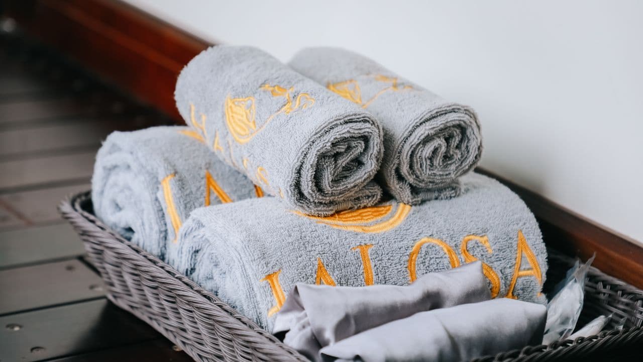 Rolled gray towels with gold embroidery stacked in a woven basket