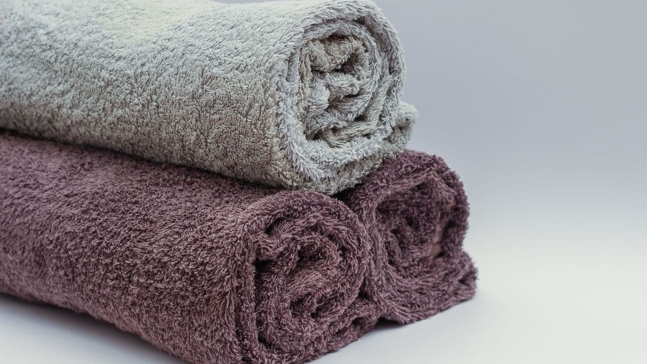 Two rolled bath towels in gray and mauve stacked on a pale surface