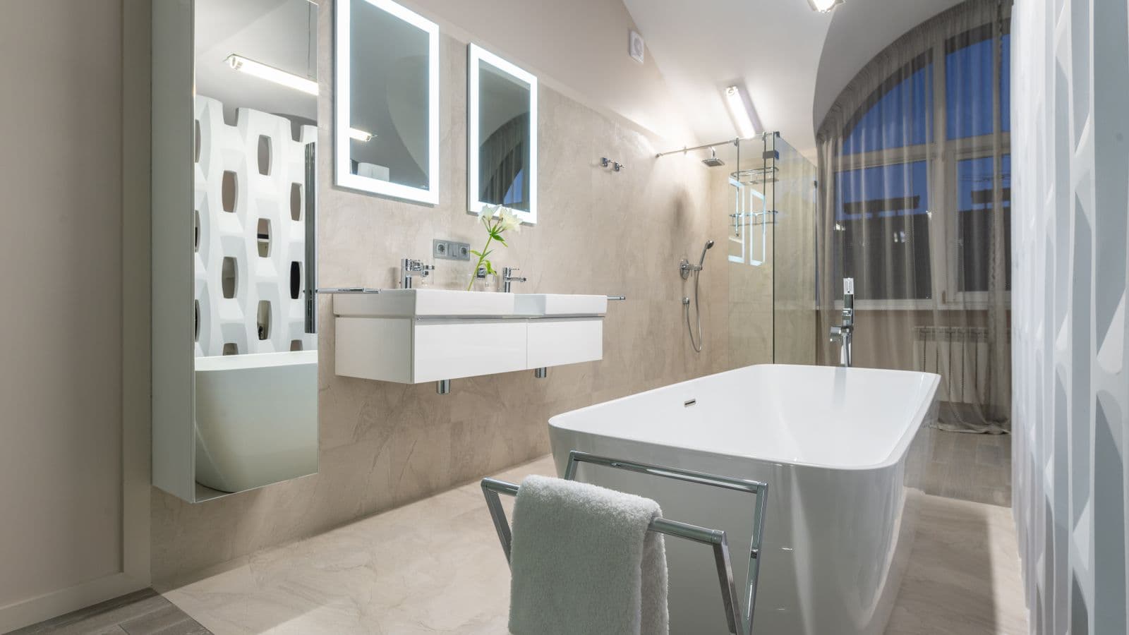 A chrome freestanding towel rail holding a folded towel beside a freestanding bathtub