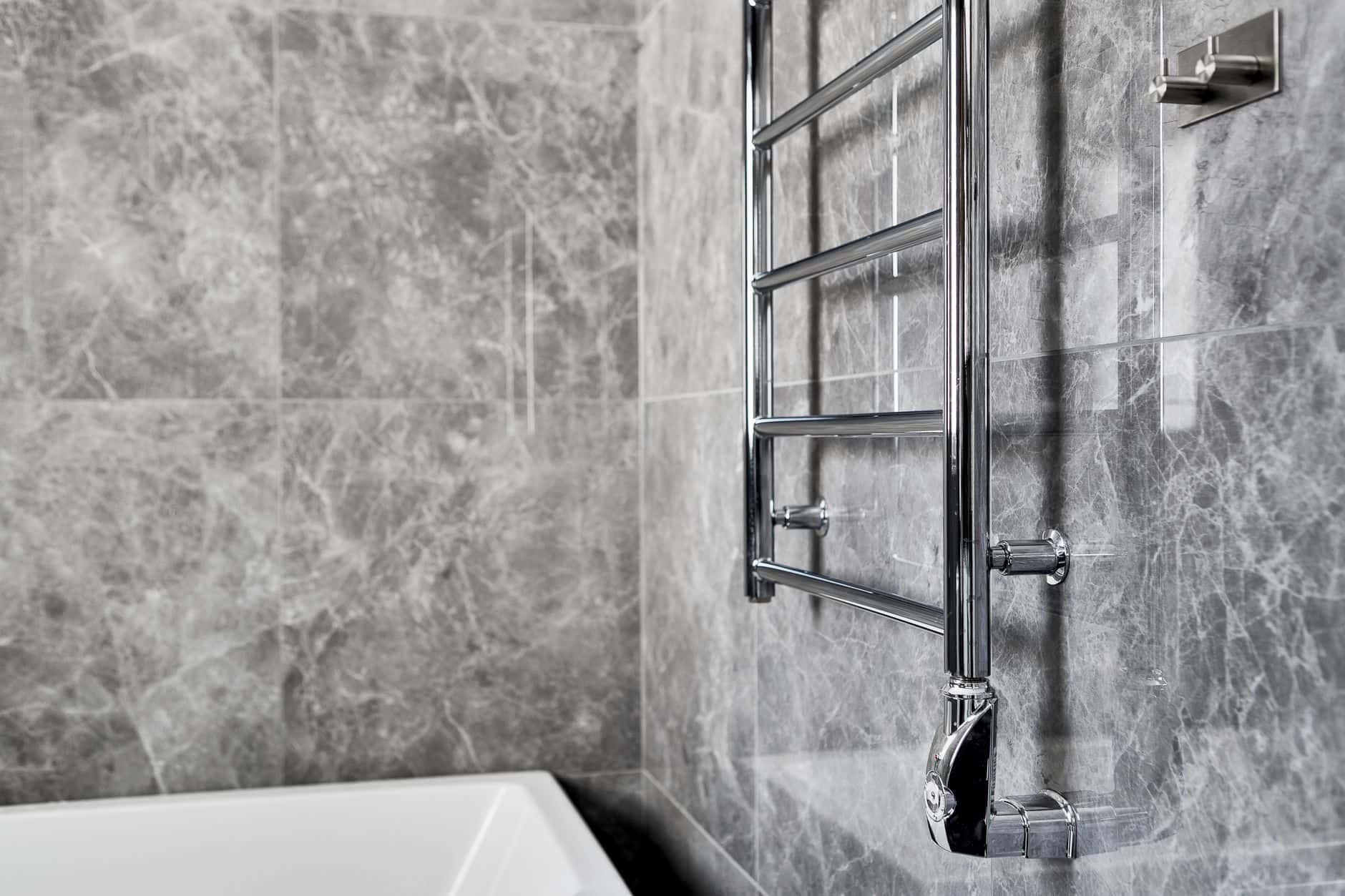 A chrome heated towel rail with four bars on a gray marble bathroom wall
