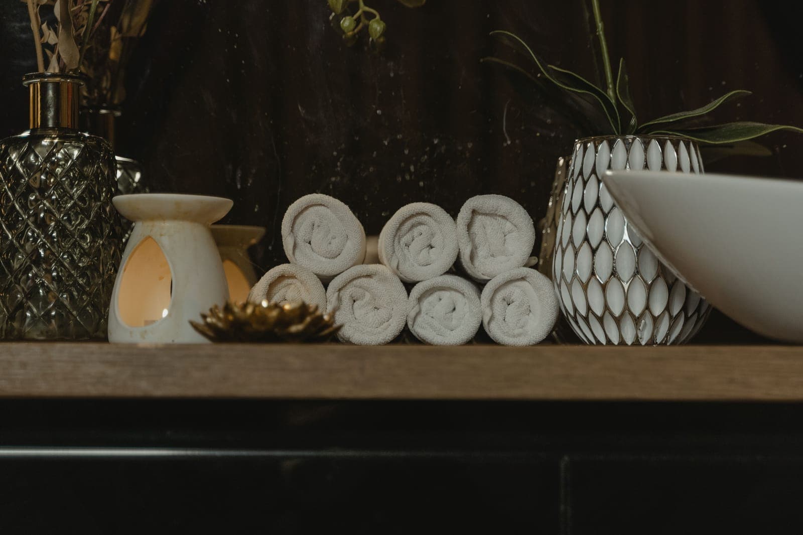 Rolled white towels stacked on a wooden shelf beside a lit candle burner